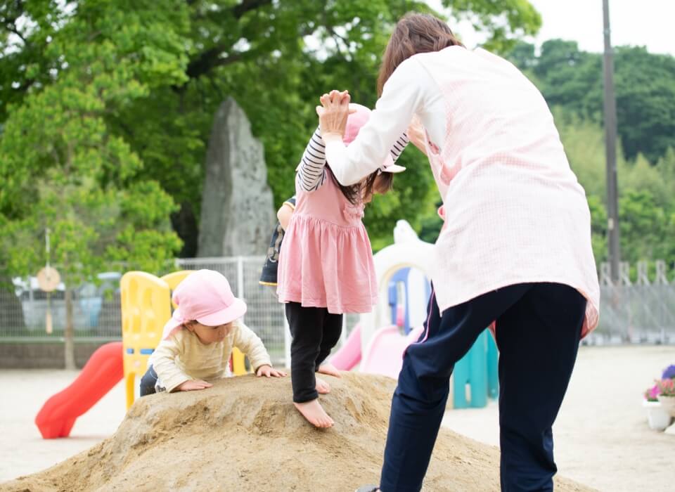 保育士が公園の砂場で子ども達と遊ぶ様子